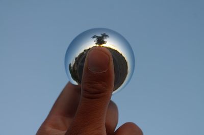 Cropped image of man holding crystal ball against sky