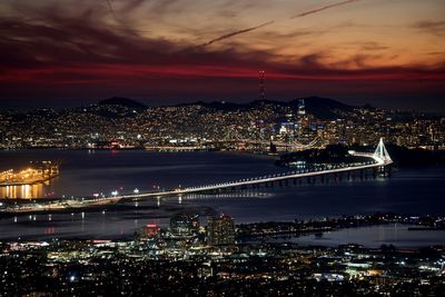 Illuminated city by river against sky at night