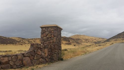 Stone wall by road against sky