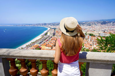 French riviera. back view of beautiful young woman holding hat enjoying the cityscape of nice,france