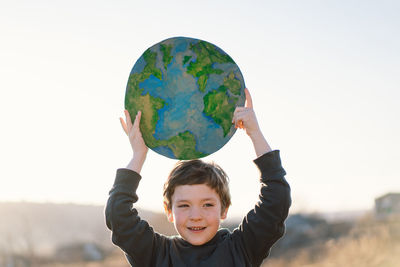 Portrait of cute boy holding globe against sky