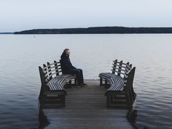 Man sitting on pier over lake against sky