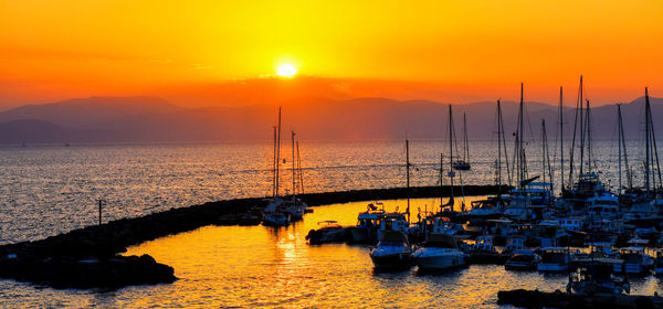 Sailboats moored on sea against sky during sunset