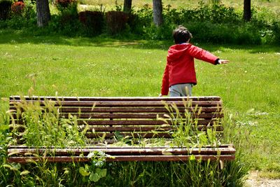 Rear view of young boy running in the park near a bench full of plants