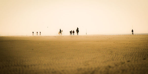 People walking on sand against clear sky