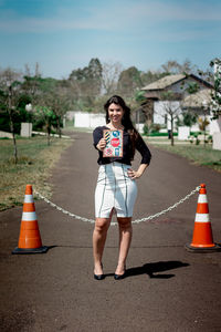 Full length portrait of young woman standing on road