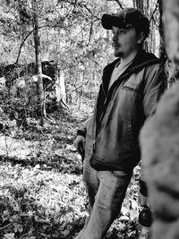 Side view of young man standing against trees