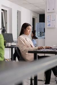 Portrait of young woman using mobile phone while standing in office