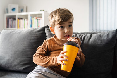 Close-up of boy drinking water on sofa at home