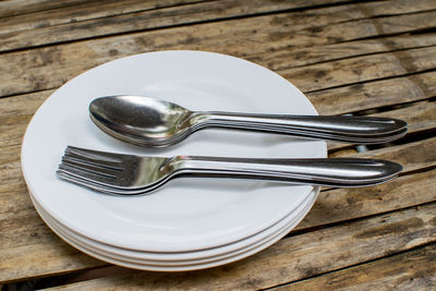 High angle view of forks and spoons with stacked plates on table