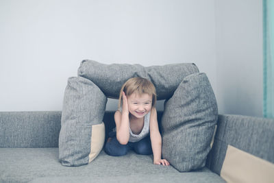 Kid toddler builds house from pillows on sofa in living room, lifestyle and games in real interior