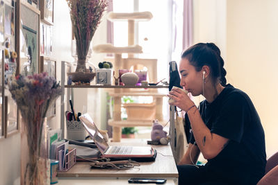 Side view of woman using phone while sitting on table