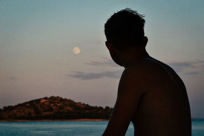 Side view of shirtless man at beach against sky during sunset