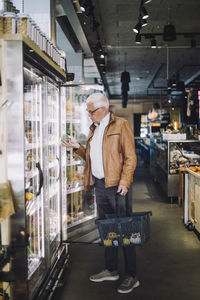 Full length of senior man analyzing organic vegetable at grocery store