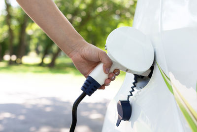 Cropped hand of woman charging electric car at station