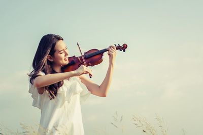 Young woman playing violin while standing against sky