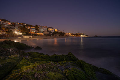 Illuminated buildings by sea against sky at night