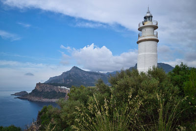 Lighthouse by sea and buildings against sky