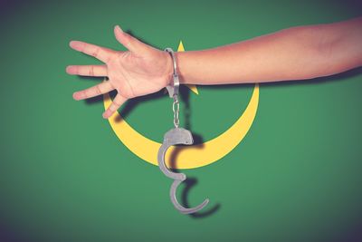 Cropped hand of person wearing handcuffs against blue background