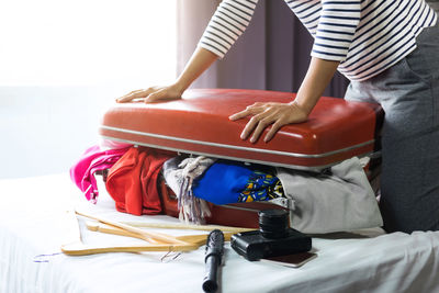 Midsection of woman packing suitcase on bed in hotel room