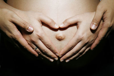 Cropped hands of couple touching belly against black background