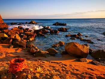 Rocks on beach against sky during sunset