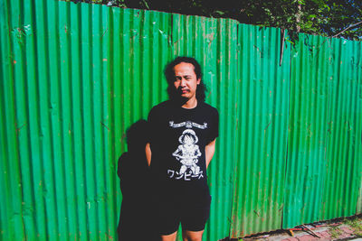 Portrait of teenage girl standing against green metal fence