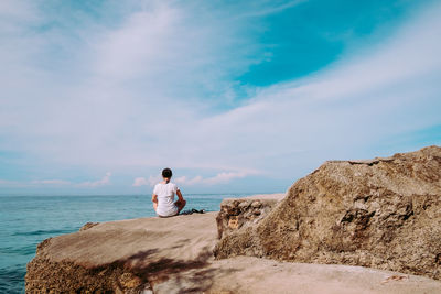 Rear view of man sitting on retaining wall at beach against sky