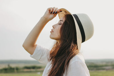 Woman wearing hat while standing on grass against sky