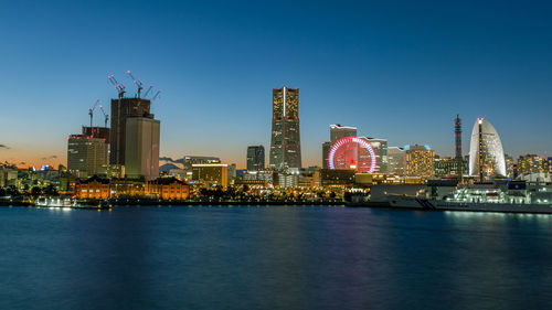 Illuminated buildings by river against clear sky
