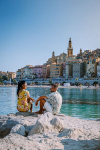 People sitting by buildings against clear sky