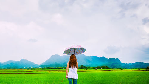 Rear view of woman standing on field against sky