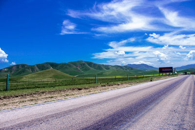 Empty road by mountains against cloudy sky