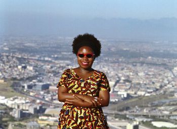 Smiling woman standing with arms crossed against city