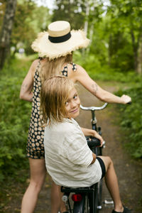 Woman with girl walking with bicycle in forest