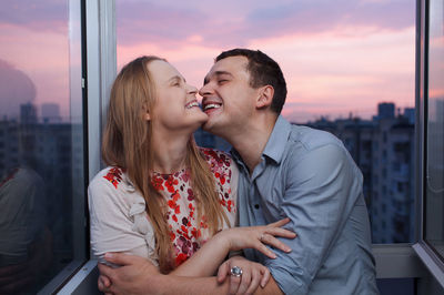 Smiling couple standing at window during sunset