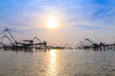 Fishing nets in sea against sky during sunset