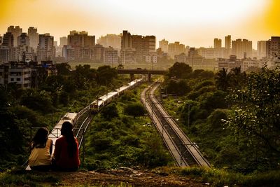 Rear view of friends sitting on mountain against sky during sunset