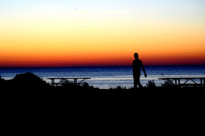 Silhouette man standing by sea against sky during sunset