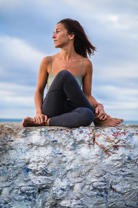 Young woman sitting on rock against sky
