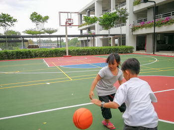 Girl playing basketball with brother at court