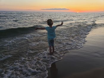 Rear view of girl standing at beach during sunset