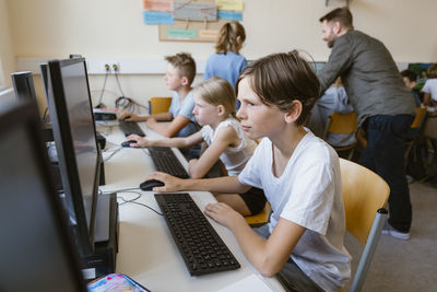 Concentrated male pupil using computer while sitting with students at desk in computer classroom