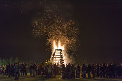 People standing by bonfire against sky at night