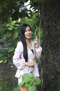 Young woman smiling while standing against tree trunk