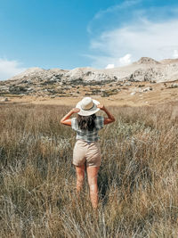 Rear view of female hiker standing in tall grass in front of rocky hills.