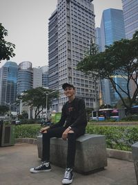 Young man sitting against modern buildings in city