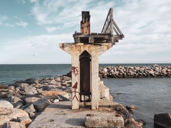 Cross on rock by sea against sky