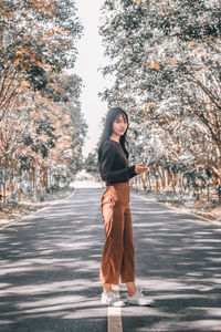 Portrait of young woman standing on road amidst trees in forest