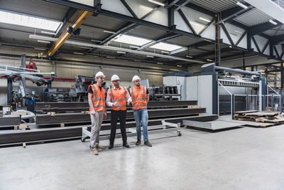 Three men wearing hard hats and safety vests talking on factory shop floor